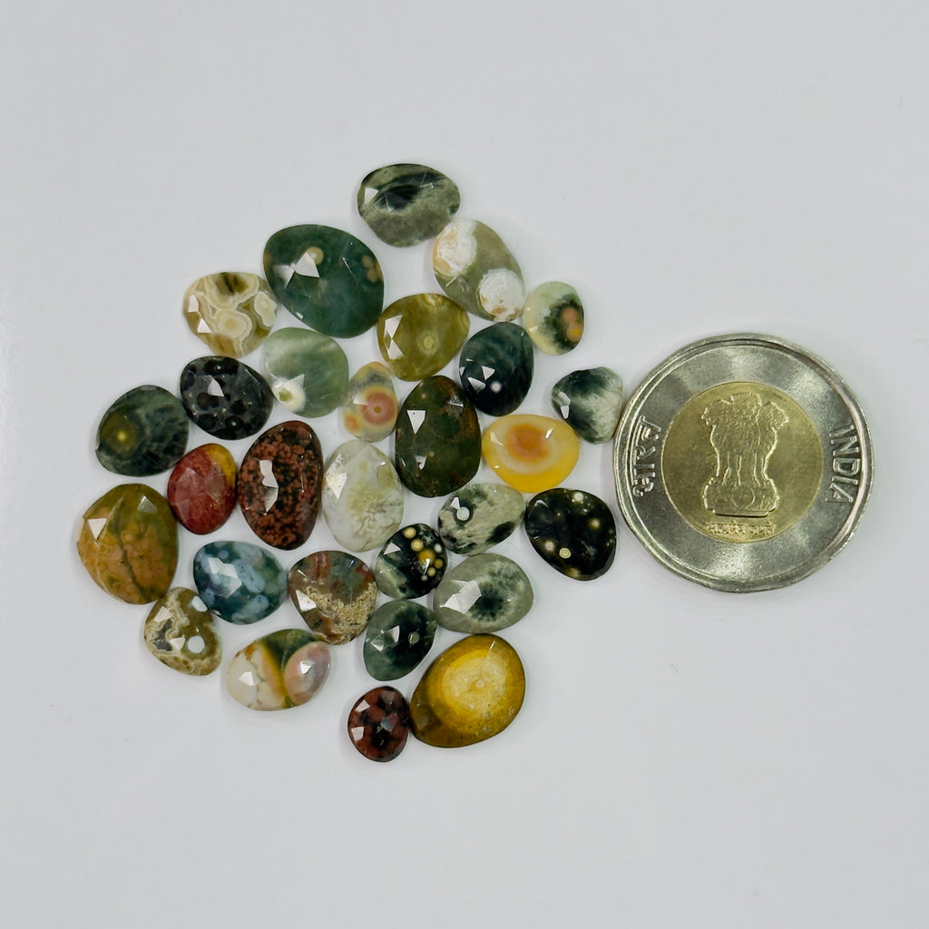 Assorted colored gemstones with a coin for scale on a white background