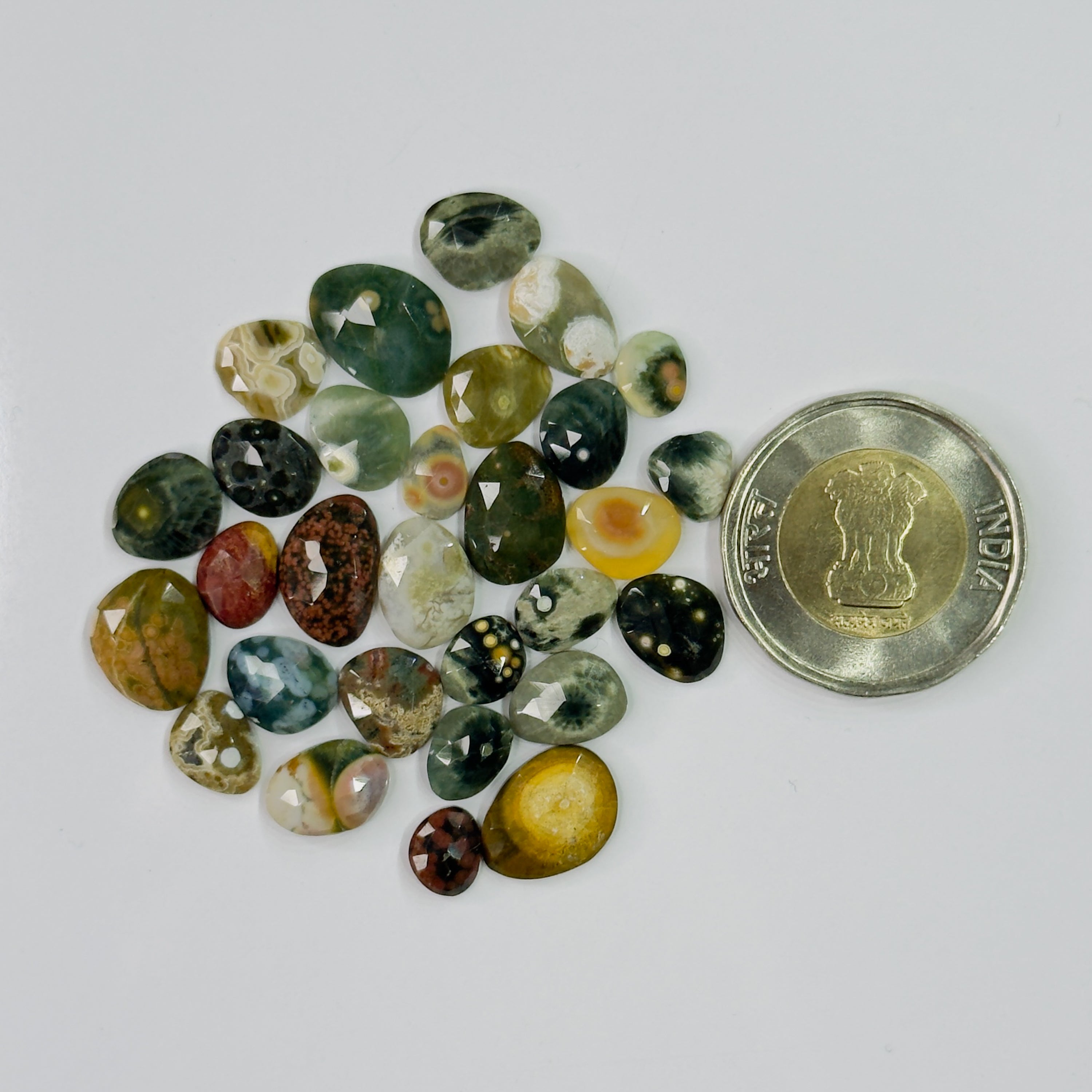 Assorted colored gemstones with a coin for scale on a white background