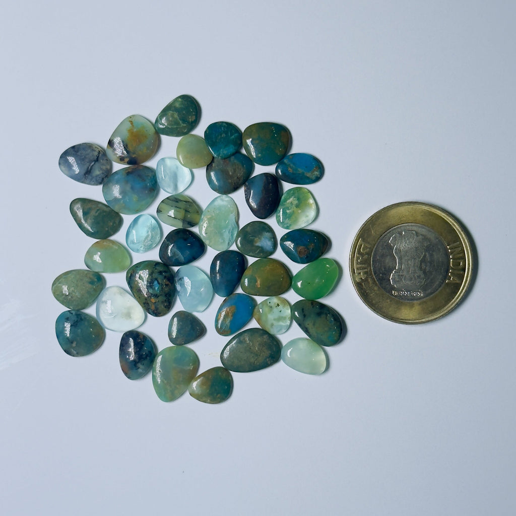 Collection of green and blue stones on a light gray background with a coin for scale.