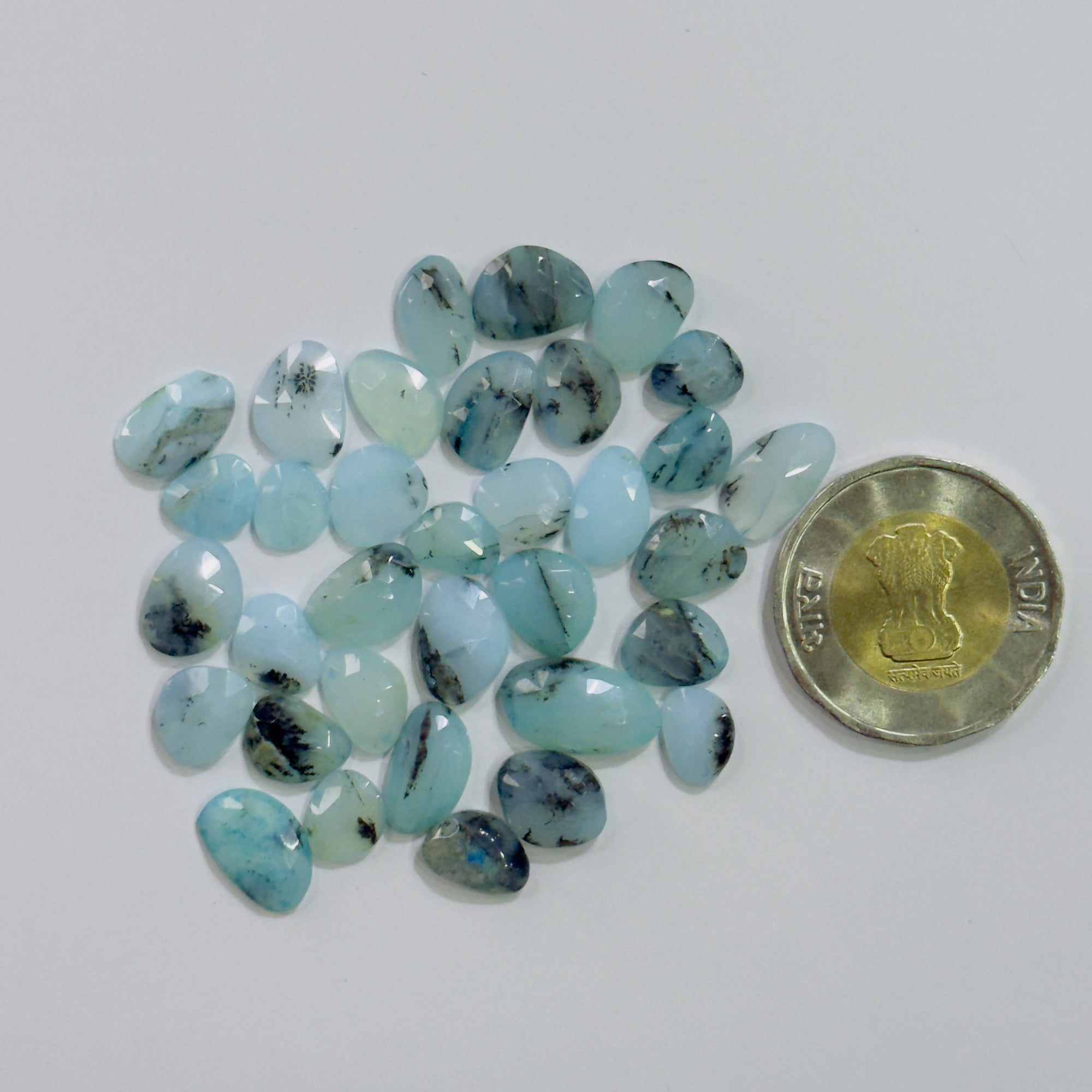 Turquoise stones with a coin for scale on a white background