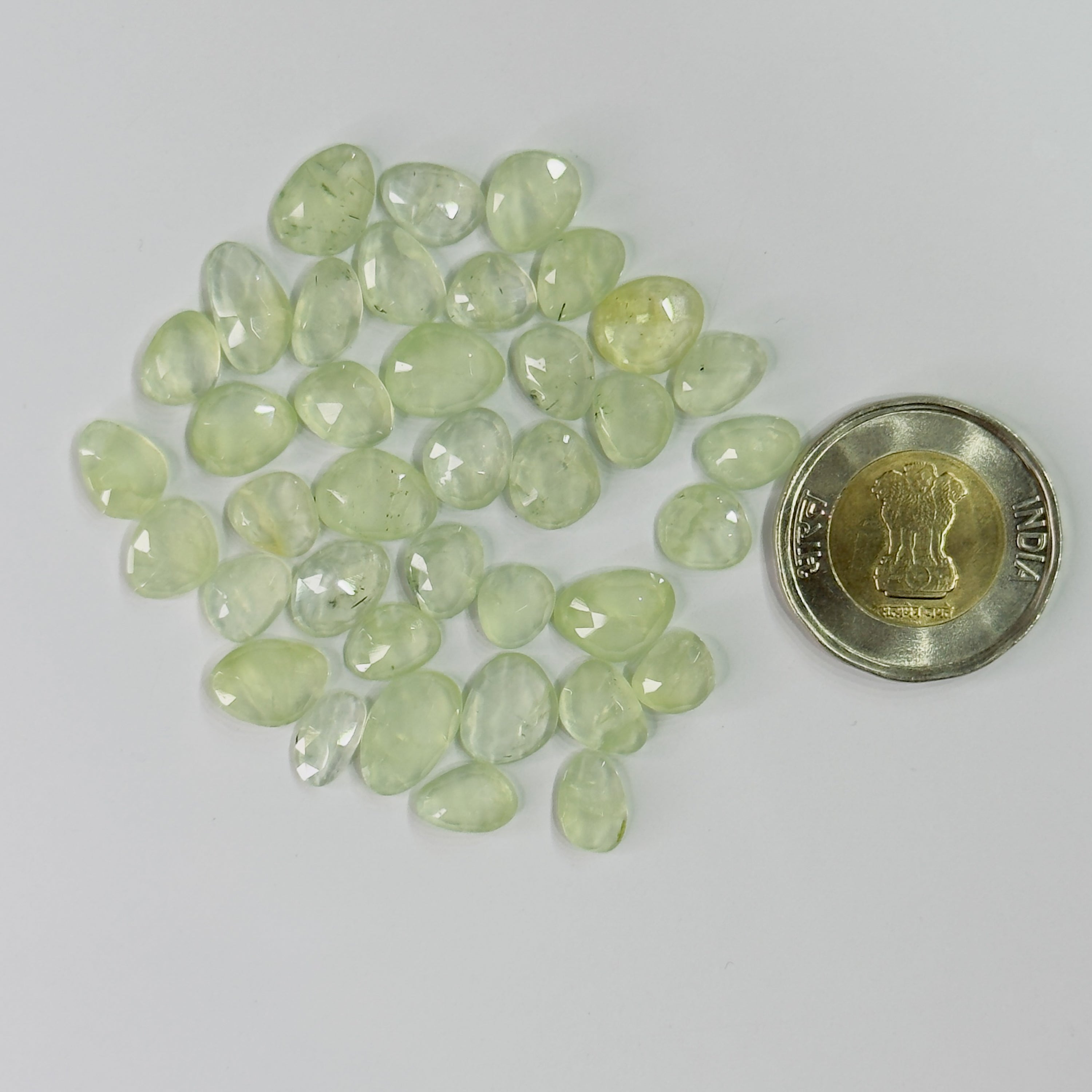 Green gemstones with a coin for scale on a gray background
