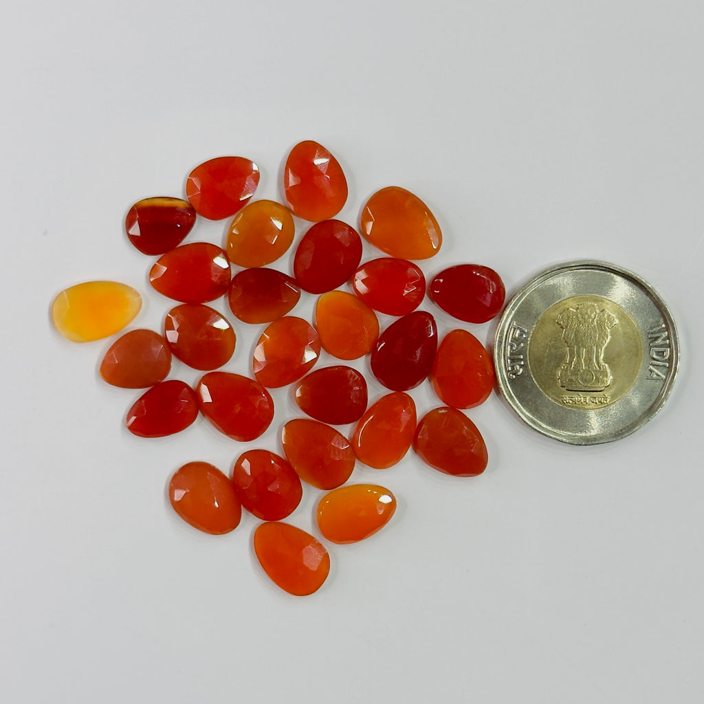 Orange and red gemstones with a coin for scale on a white background