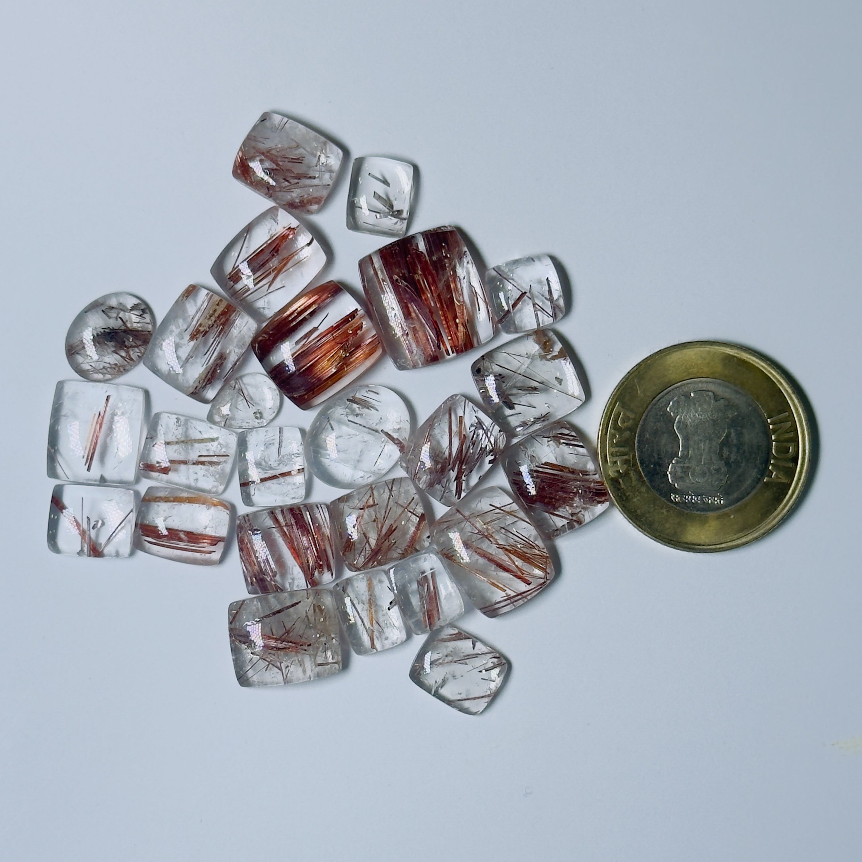 Collection of transparent and Red gemstones with a coin for scale on a White background