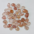 A group of polished peach and pink tumbled gemstones with natural inclusions, arranged in a loose pile on a white background.