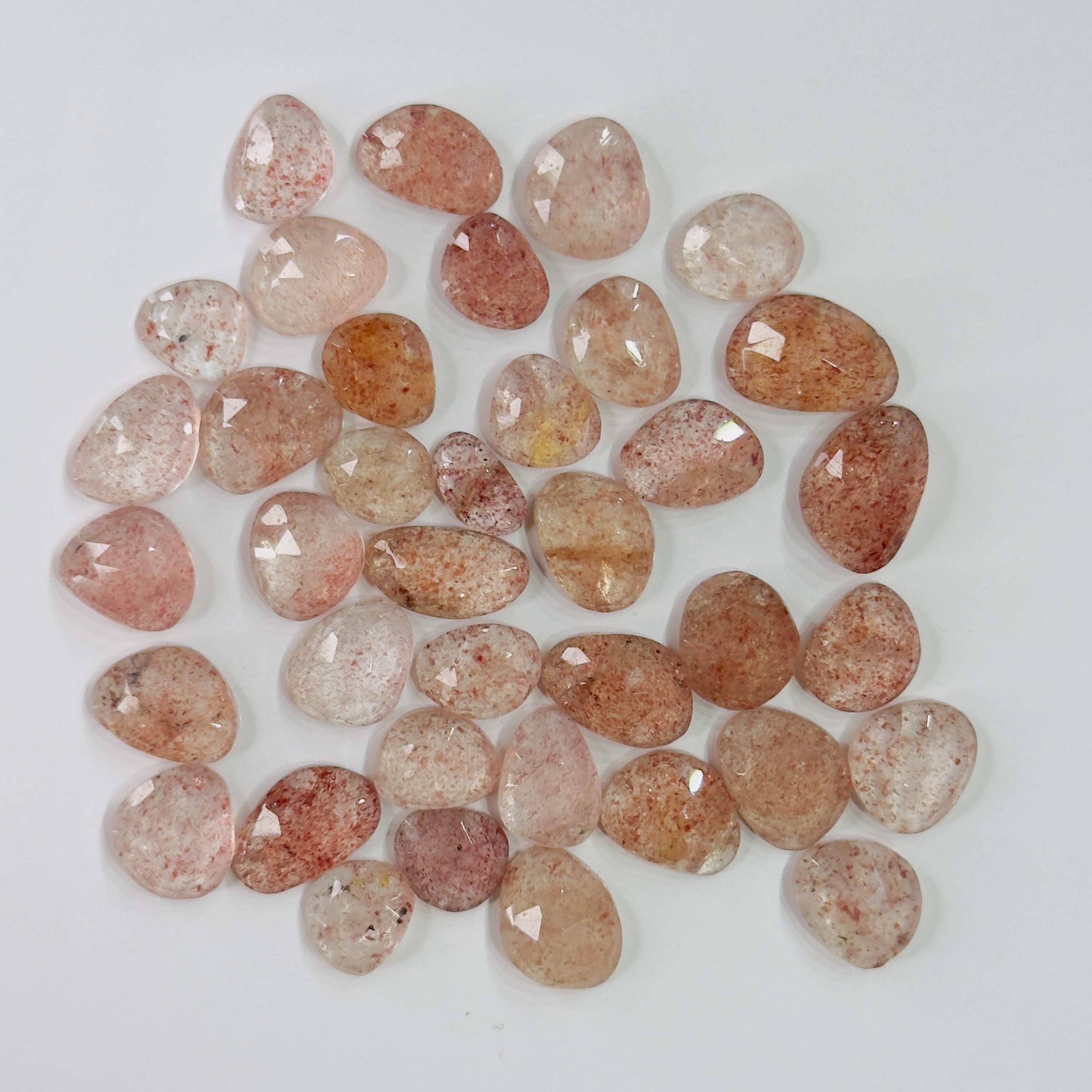 A group of polished peach and pink tumbled gemstones with natural inclusions, arranged in a loose pile on a white background.