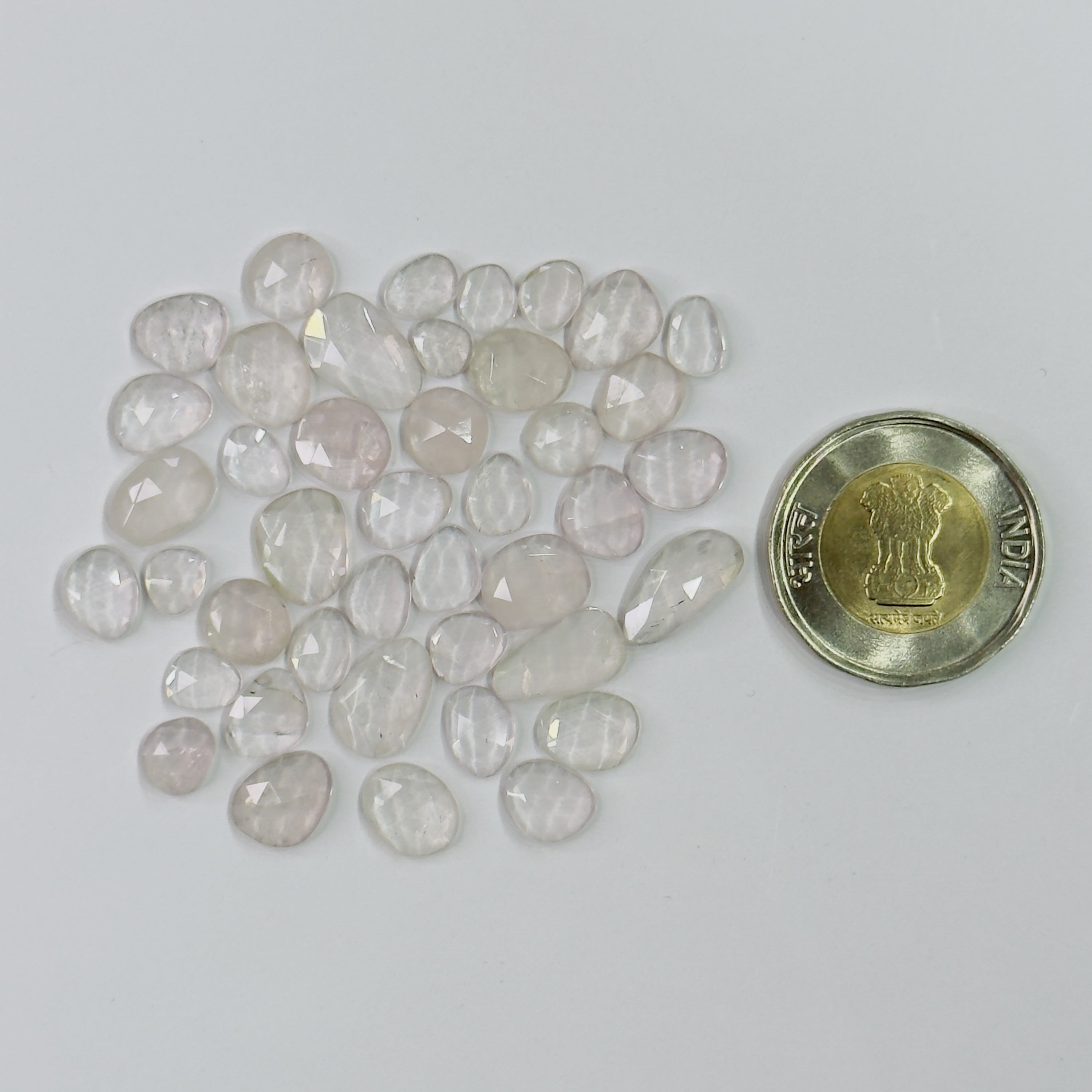 Collection of rose quartz stones with a coin for size comparison on a light gray background