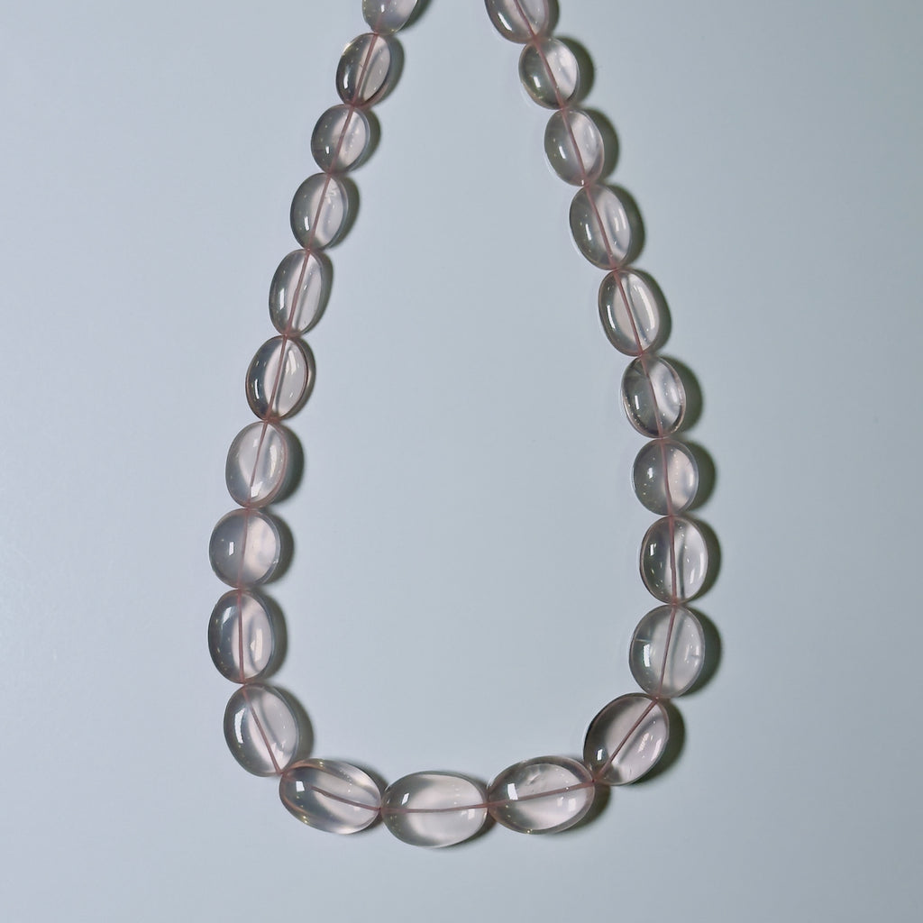 A beaded necklace made of translucent oval beads with a soft pinkish-gray hue, arranged in a teardrop shape against a light gray background.