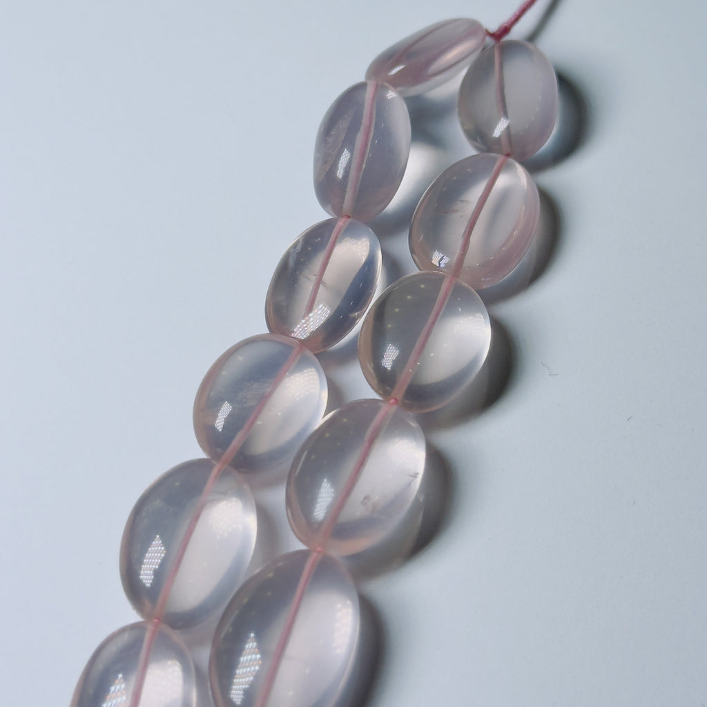 A strand of translucent pale pink oval beads strung on a pink thread, photographed on a light gray background.