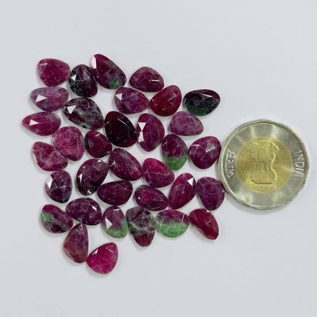Collection of red and green gemstones with a coin for scale on a white background