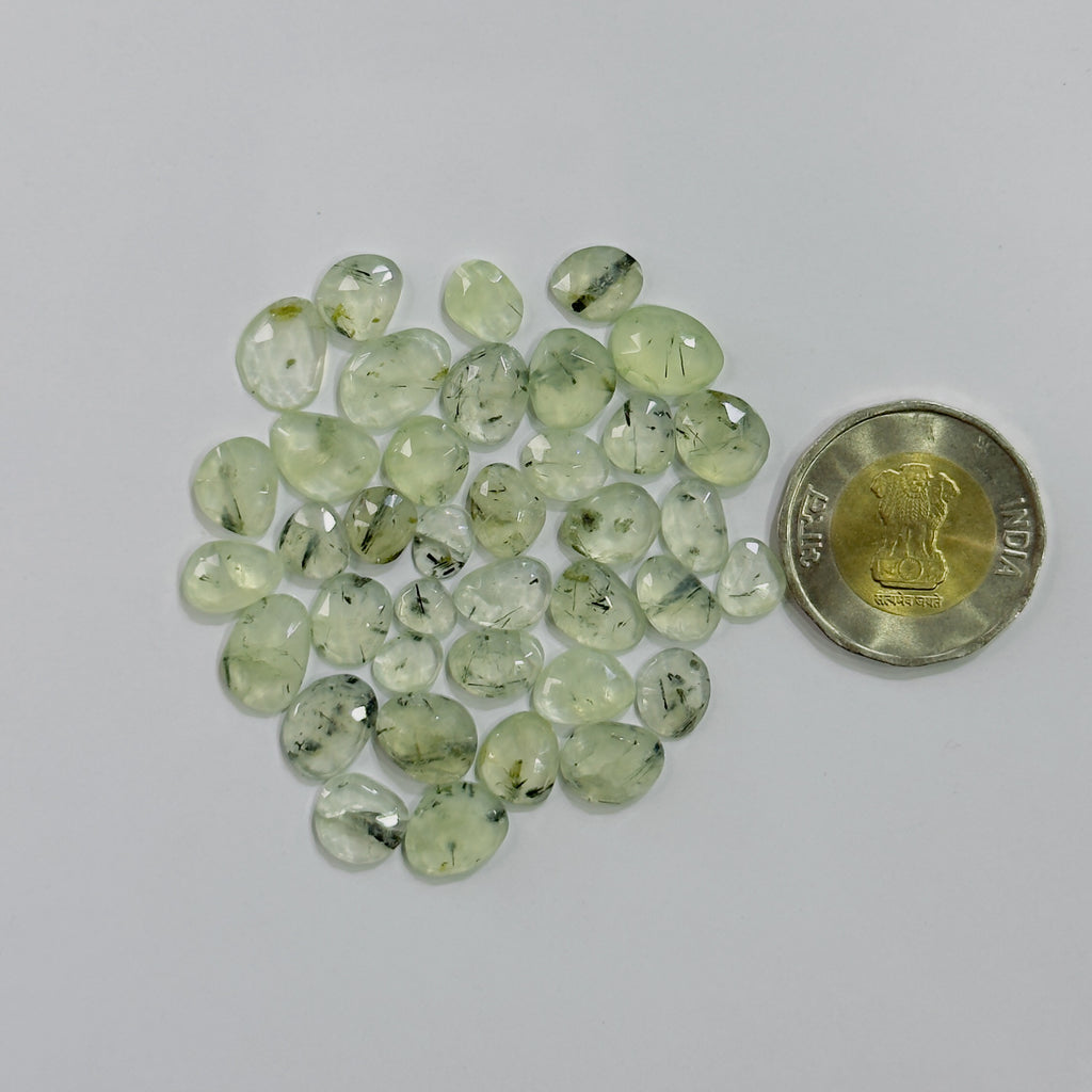Green gemstones with a coin for scale on a white background