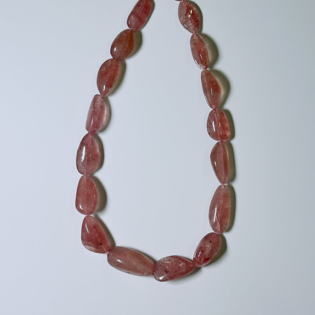 A beaded necklace made of polished, teardrop-shaped pinkish-red translucent gemstone beads, arranged in a U-shape on a plain light gray background.