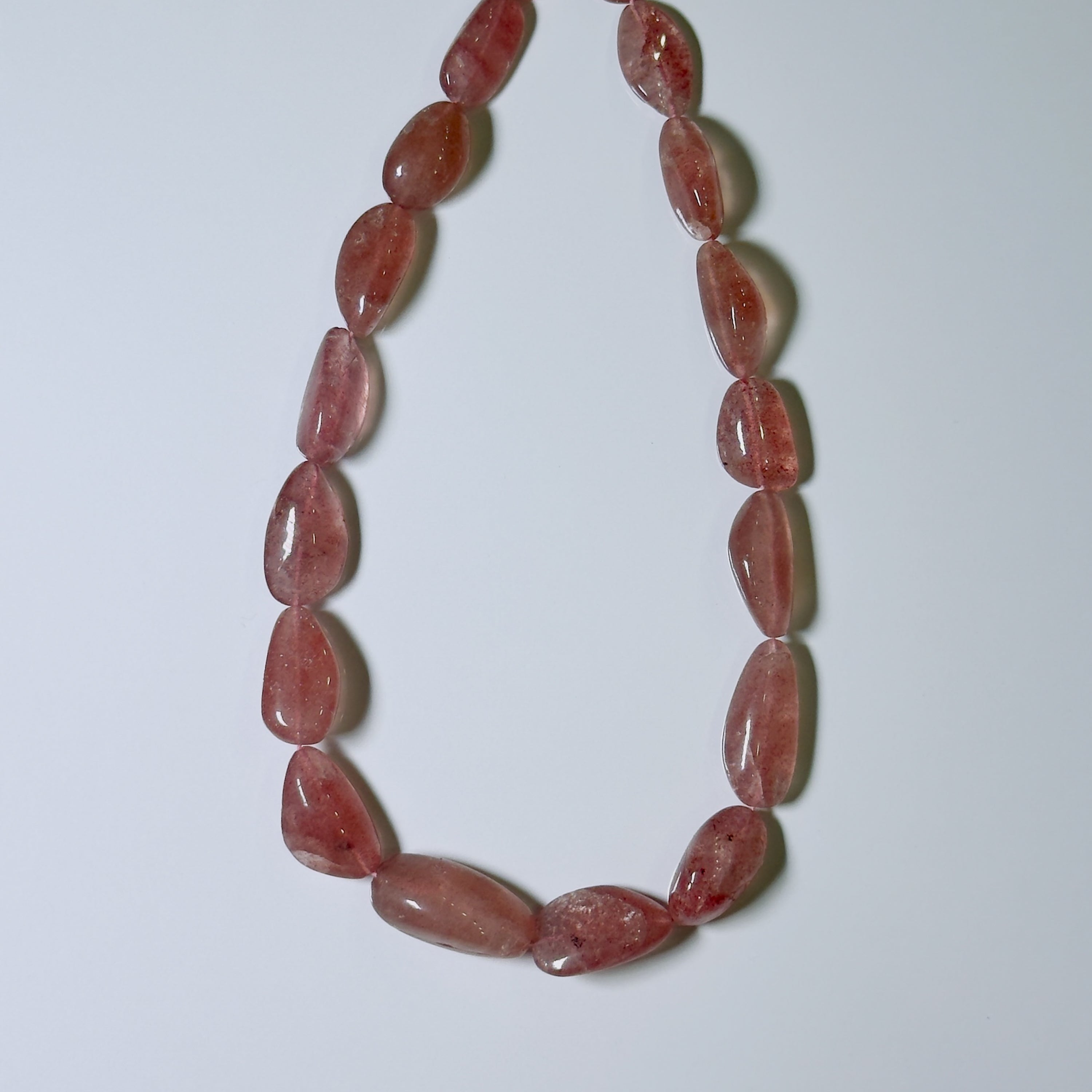 A beaded necklace made of polished, teardrop-shaped pinkish-red translucent gemstone beads, arranged in a U-shape on a plain light gray background.