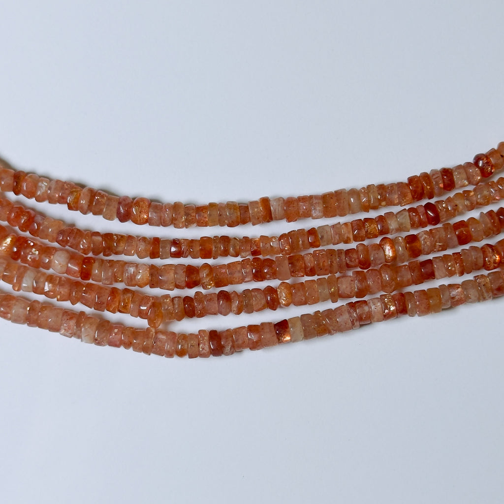 Three strands of orange beads on a light gray background