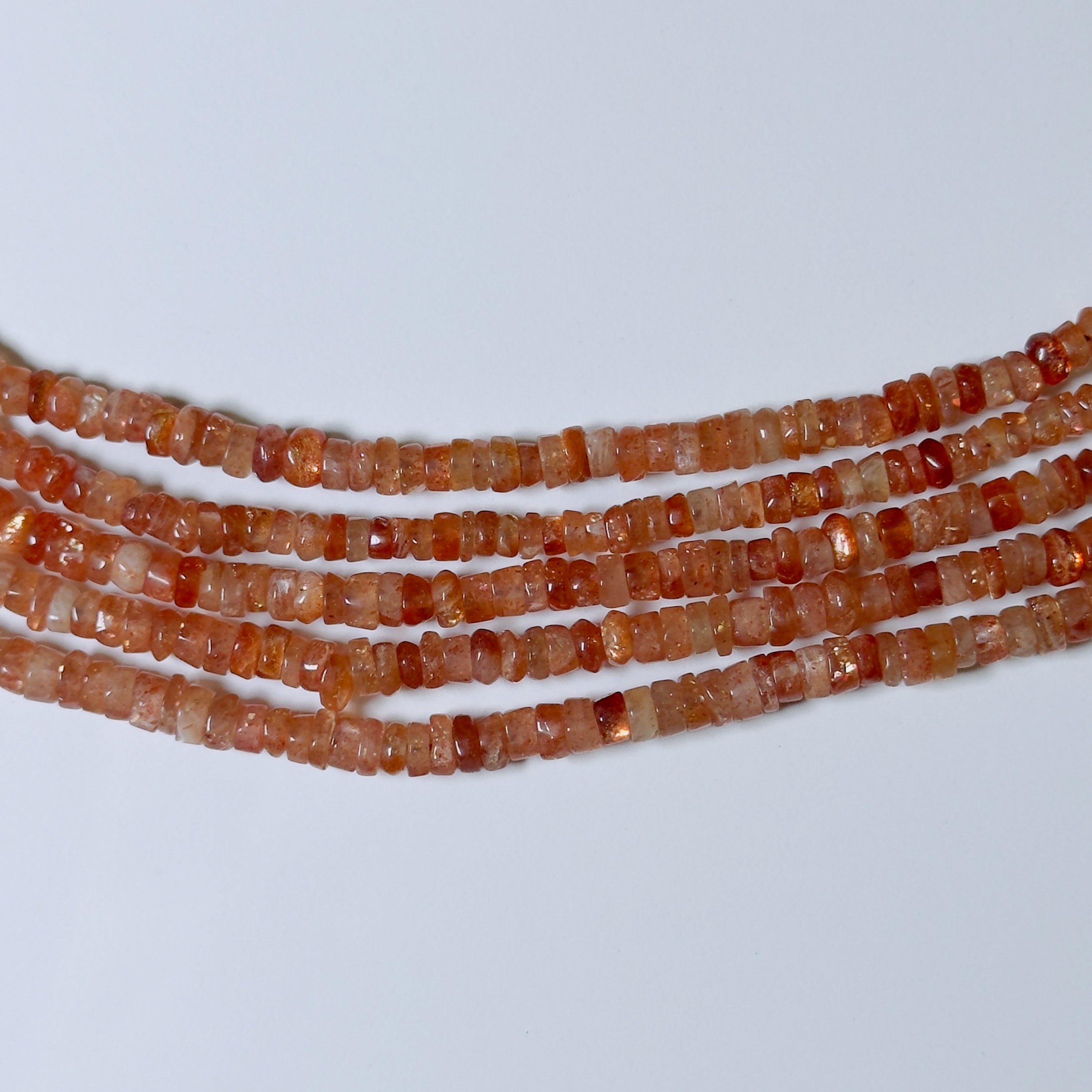 Three strands of orange beads on a light gray background