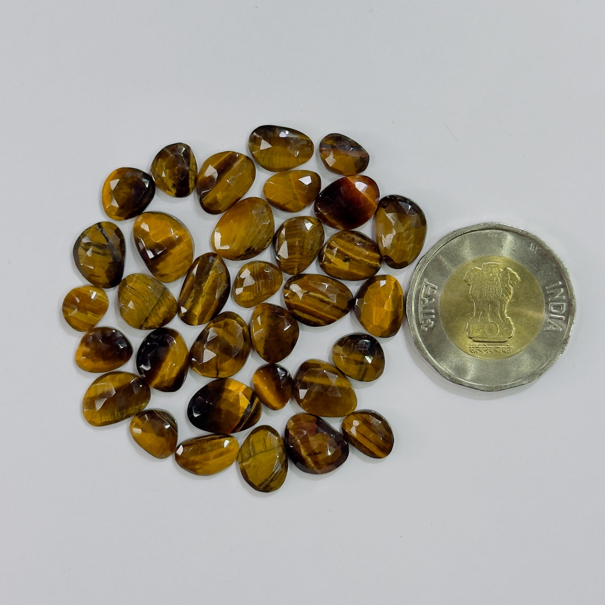 Collection of tiger eye stones with a coin for size comparison on a white background