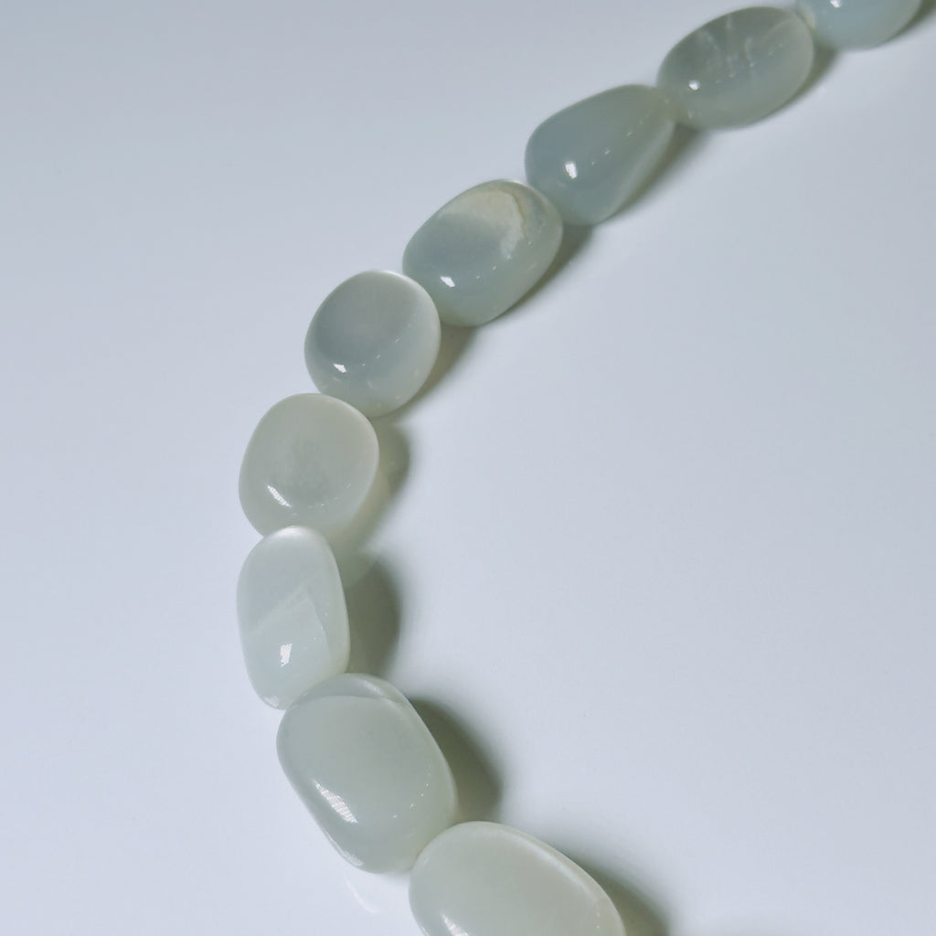 A close-up of a curved strand of polished, smooth tumbled stone beads in a pale icy blue-green hue on a clean white background.