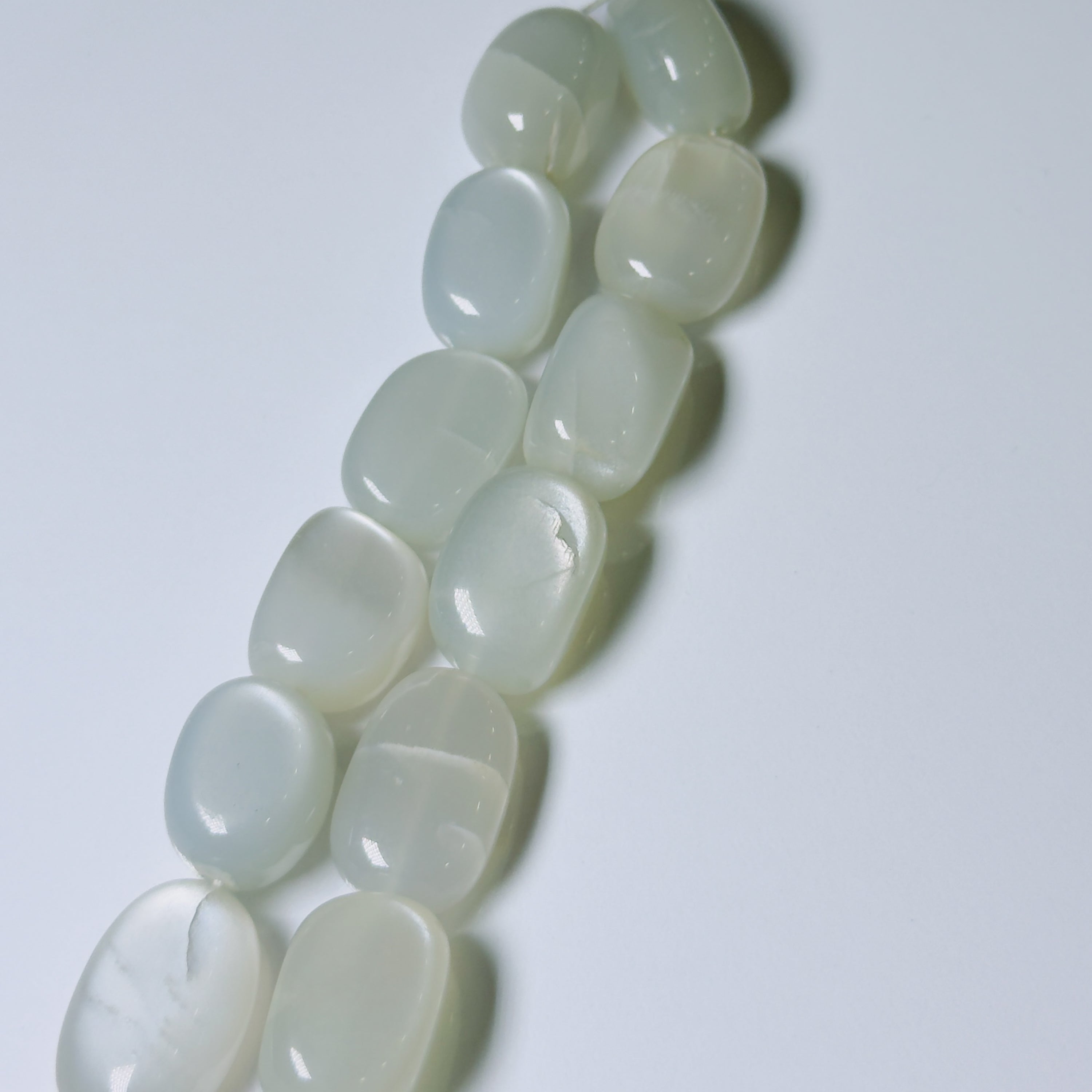 A strand of smooth, polished white stone beads with a milky, semi-translucent finish, arranged diagonally on a plain light gray background.
