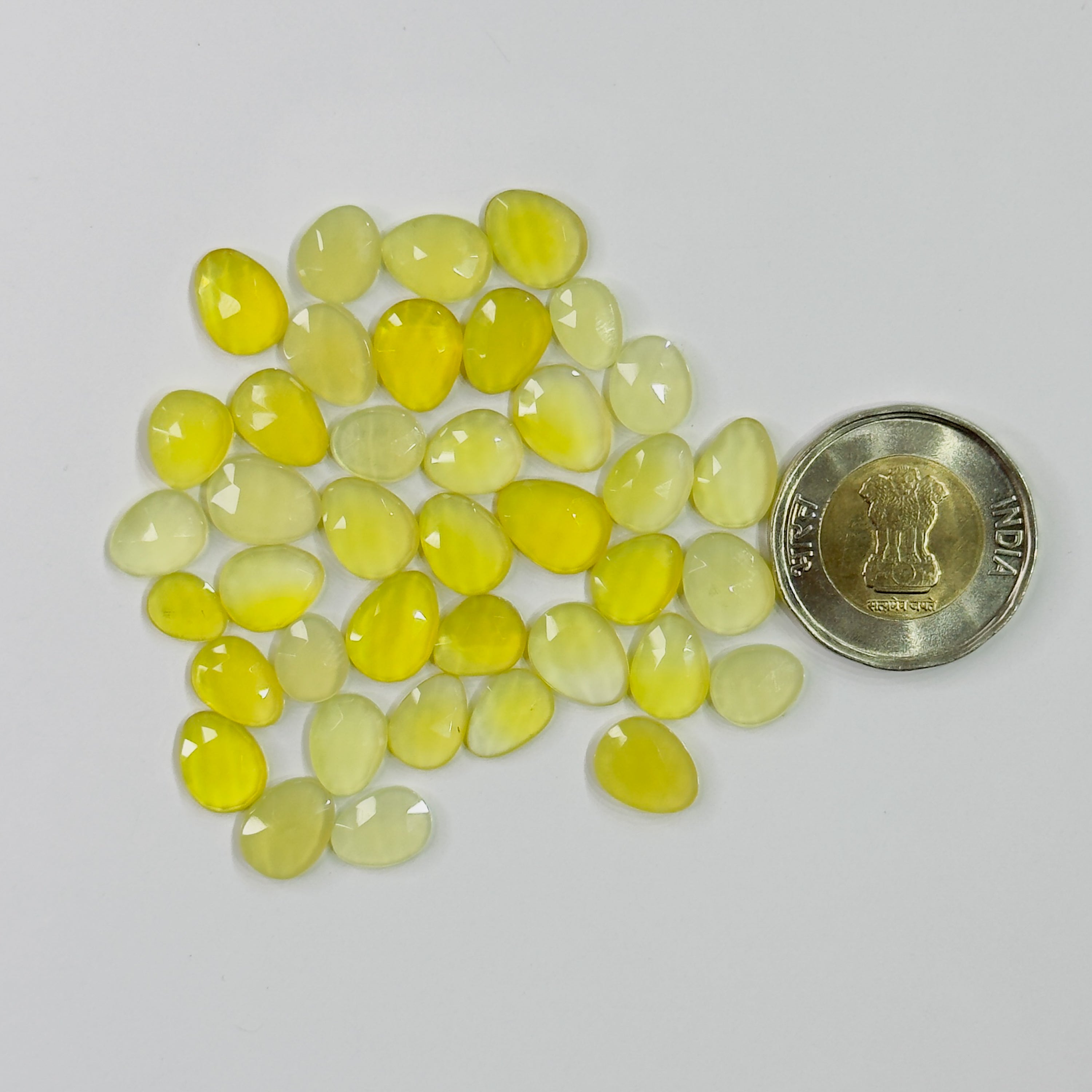 Yellow gemstones with a coin for scale on a white background